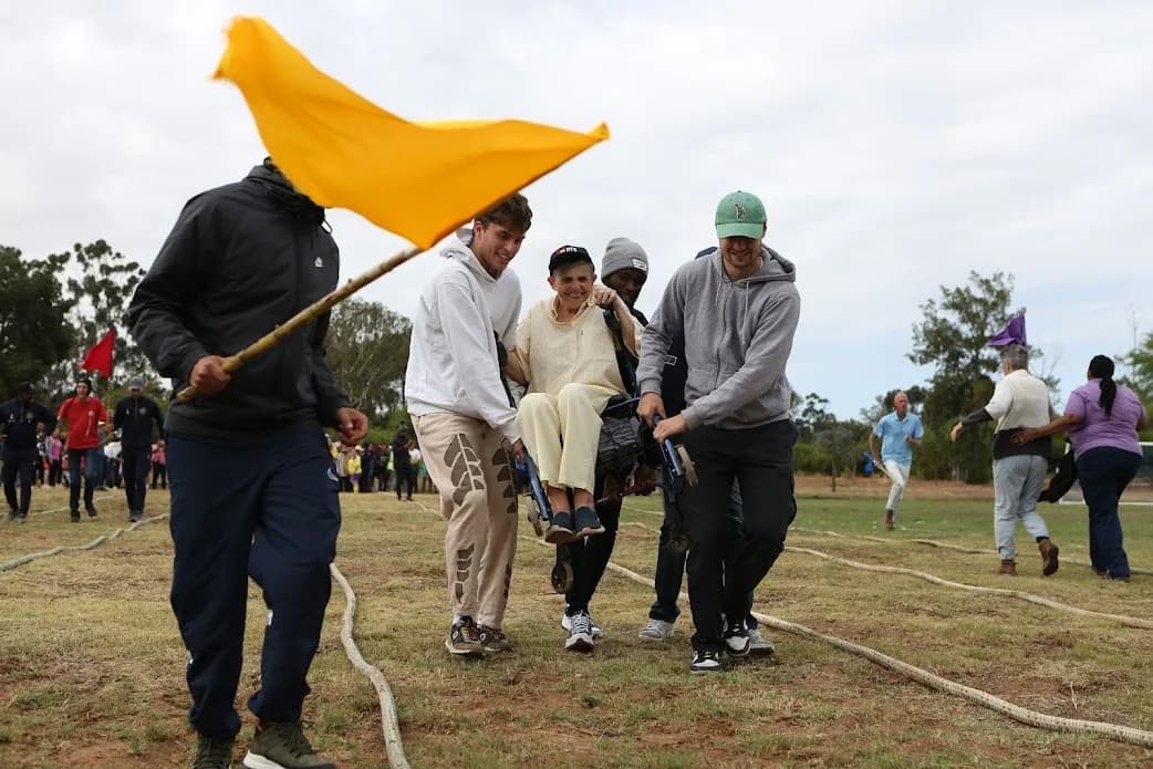 Residents, co-workers and volunteers carrying a flag across the field together on Camphill sports day
