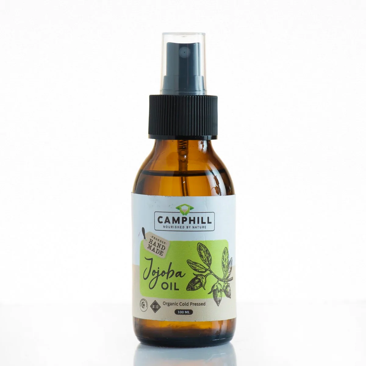 Amber glass pump bottle of Camphill Naturals jojoba oil with a green jojoba sprig on the label