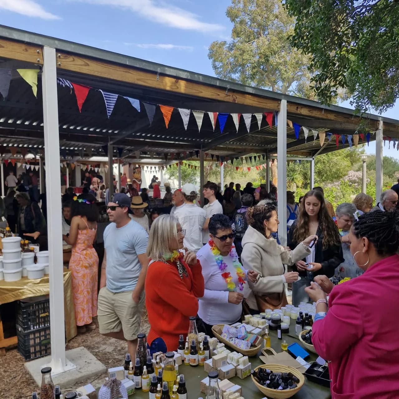 Visitors browsing a table of Camphill bottles, soaps and preserves under strings of bunting at the country market.